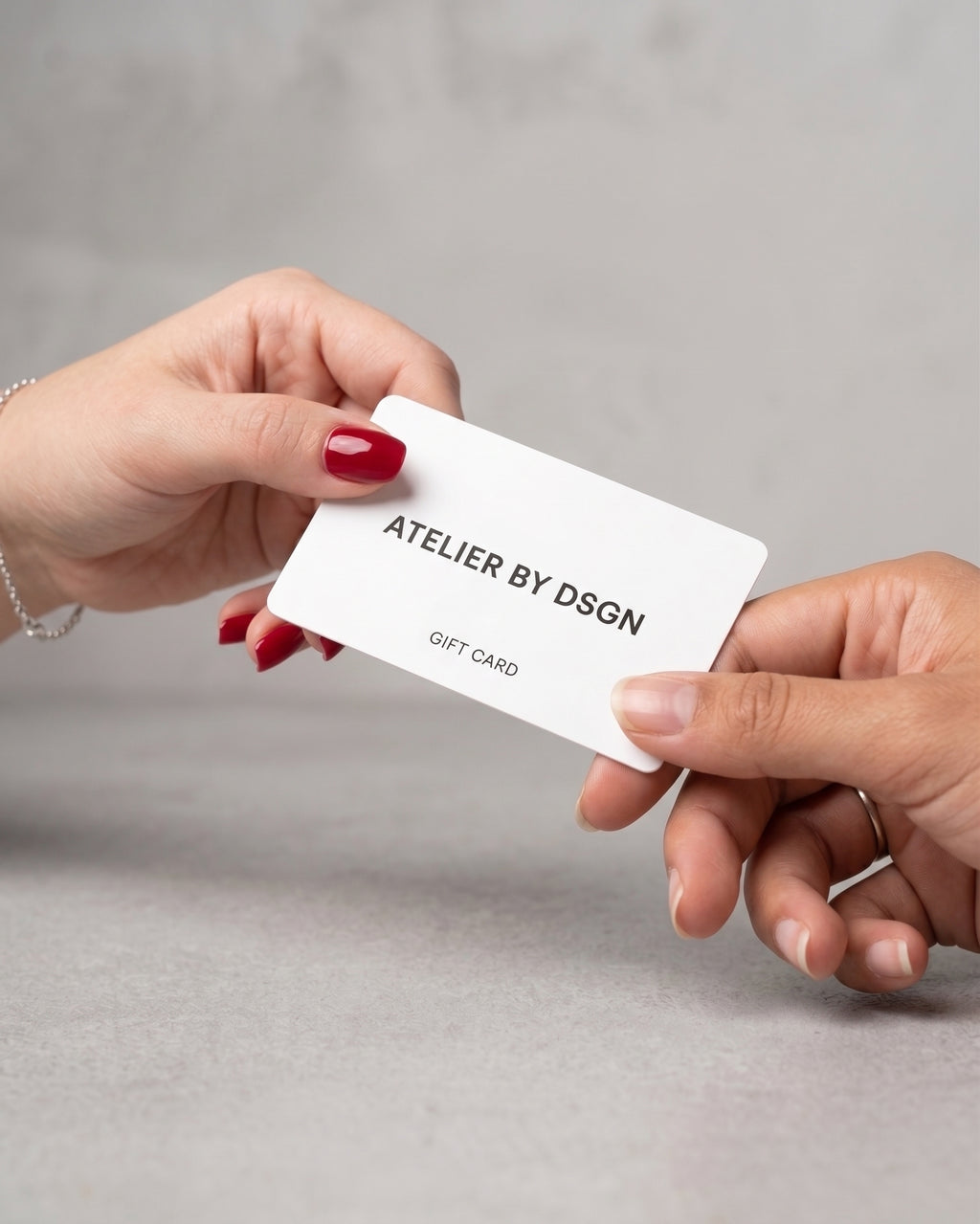 A lady giving an Atelier By DSGN Gift Card to another lady as a gift.  E-Gift Card from Atelier By DSGN.