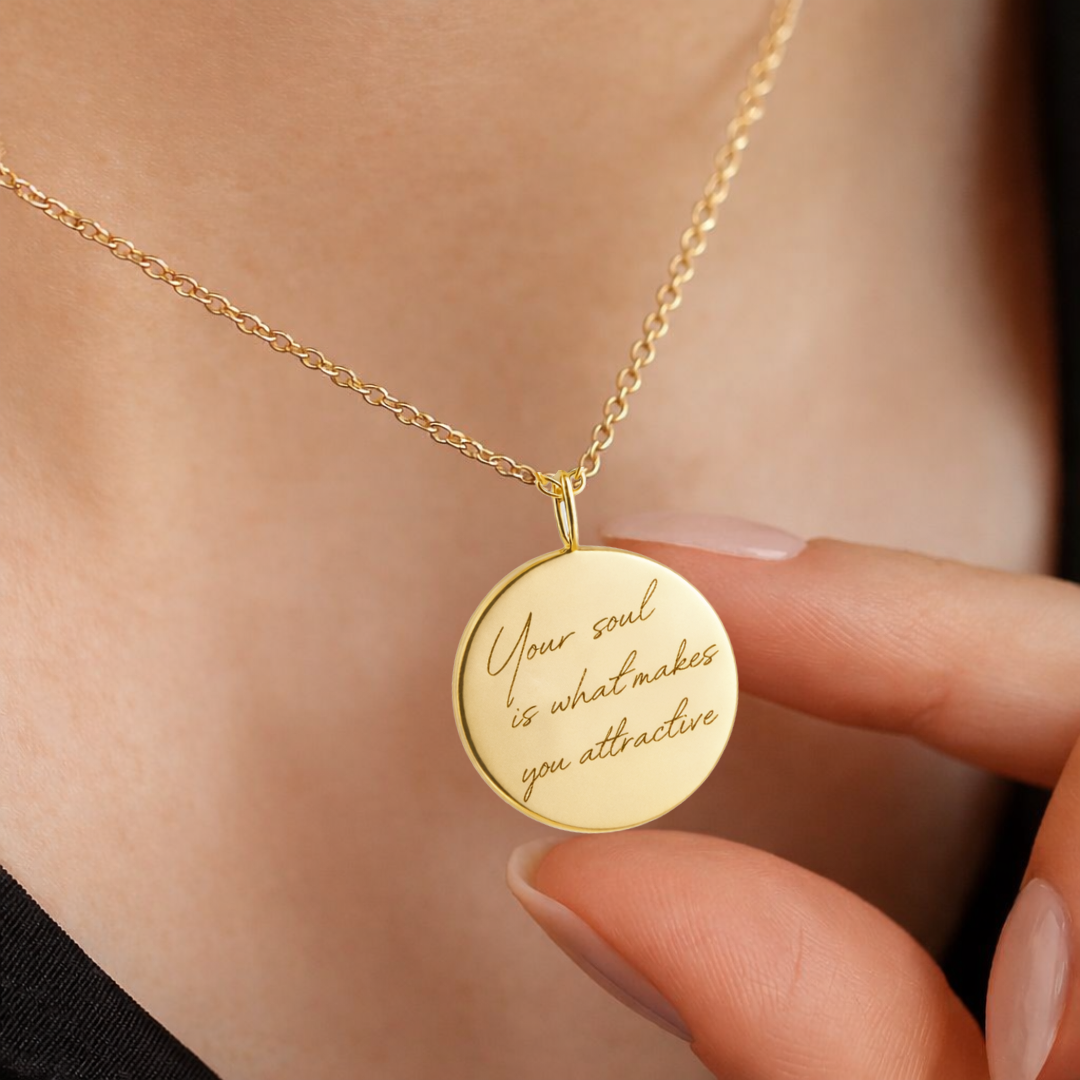 Female model holding custom engraved 18k gold vermeil 16mm coin pendant necklace at neckline displaying personalised handwriting "your soul is what makes you attractive" precision diamond-head engraved on warm lustrous gold disc on delicate gold cable chain – Atelier By Dsgn luxury personalised handwriting jewellery gift for her, birthday, anniversary or empowering sentimental keepsake necklace
