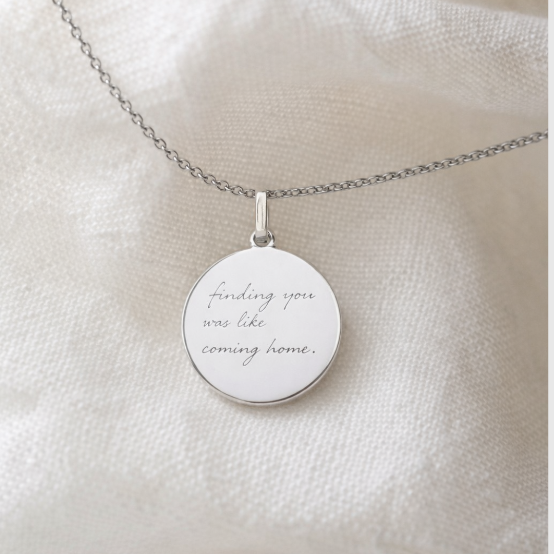 Custom engraved 925 sterling silver handwriting coin pendant necklace laid on soft white fabric, personalised handwritten message "finding you was like coming home" faithfully diamond-head engraved on polished round disc – Atelier By Dsgn personalised handwriting jewellery elegant gift for her, bride, anniversary or meaningful sympathy keepsake necklace