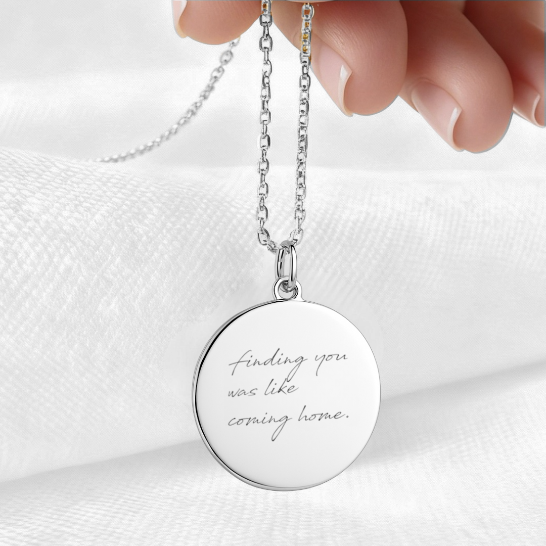 Custom engraved 925 sterling silver handwriting coin pendant necklace held against soft white fabric, personalised handwritten message "finding you was like coming home" faithfully diamond-head engraved on polished round disc – Atelier By Dsgn personalised handwriting jewellery elegant gift for her, bride, anniversary or meaningful sympathy keepsake necklace