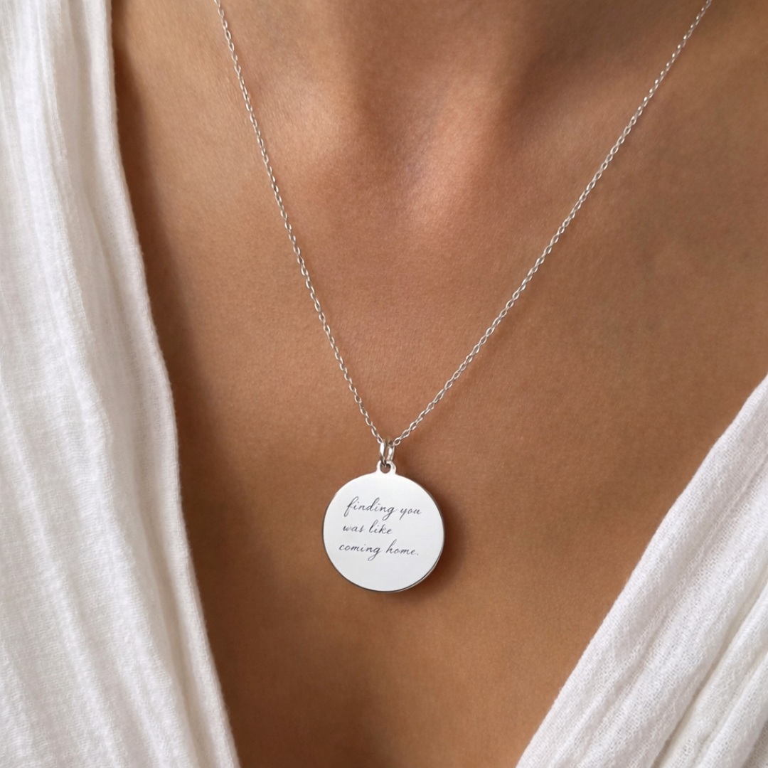 Custom engraved 925 sterling silver handwriting coin pendant necklace worn at neckline on female model in white top, personalised handwritten message "finding you was like coming home" precision engraved on polished round disc on delicate diamond-cut cable chain – Atelier By Dsgn personalised jewellery gift for her, anniversary, mothers day or valentines day keepsake necklace