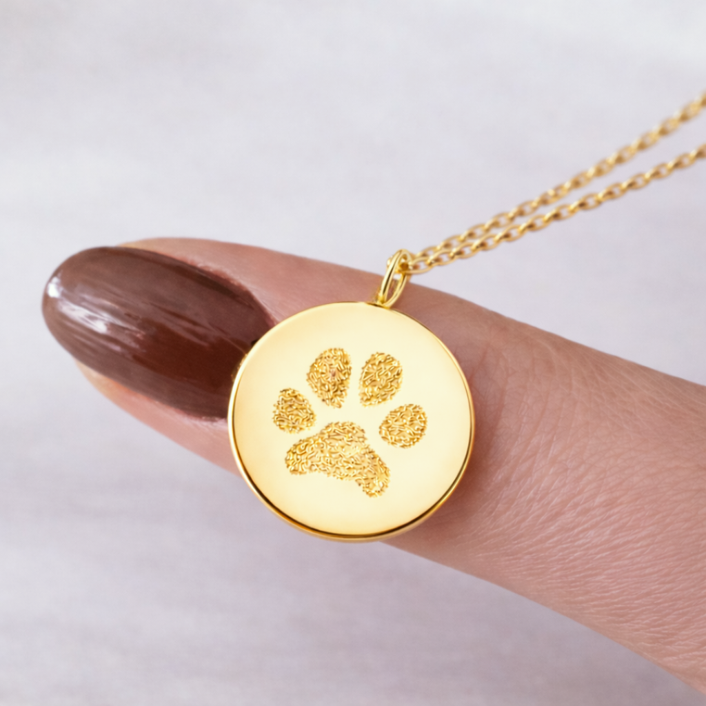 Close-up of custom engraved 18k gold vermeil 16mm coin pendant necklace balanced on female fingertip, showcasing intricate personalised pet paw print texture precision diamond-head engraved on warm polished gold disc – Atelier By Dsgn personalised paw print jewellery thoughtful gift for dog mum, cat mum, pet lover, memorial keepsake or rainbow bridge remembrance necklace