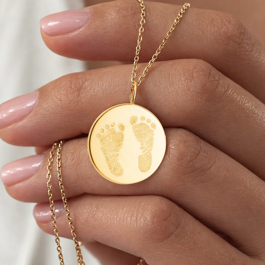 Close-up of custom engraved 18k gold vermeil 16mm coin pendant necklace resting in female palm with nude nails, showcasing intricate personalised double newborn baby footprints with detailed toe and sole texture precision diamond-head engraved on warm lustrous gold disc on delicate gold diamond-cut cable chain – Atelier By Dsgn luxury custom footprint coin necklace cherished gift for new mum, mothers day, baby shower, birth announcement or treasured newborn family heirloom necklace