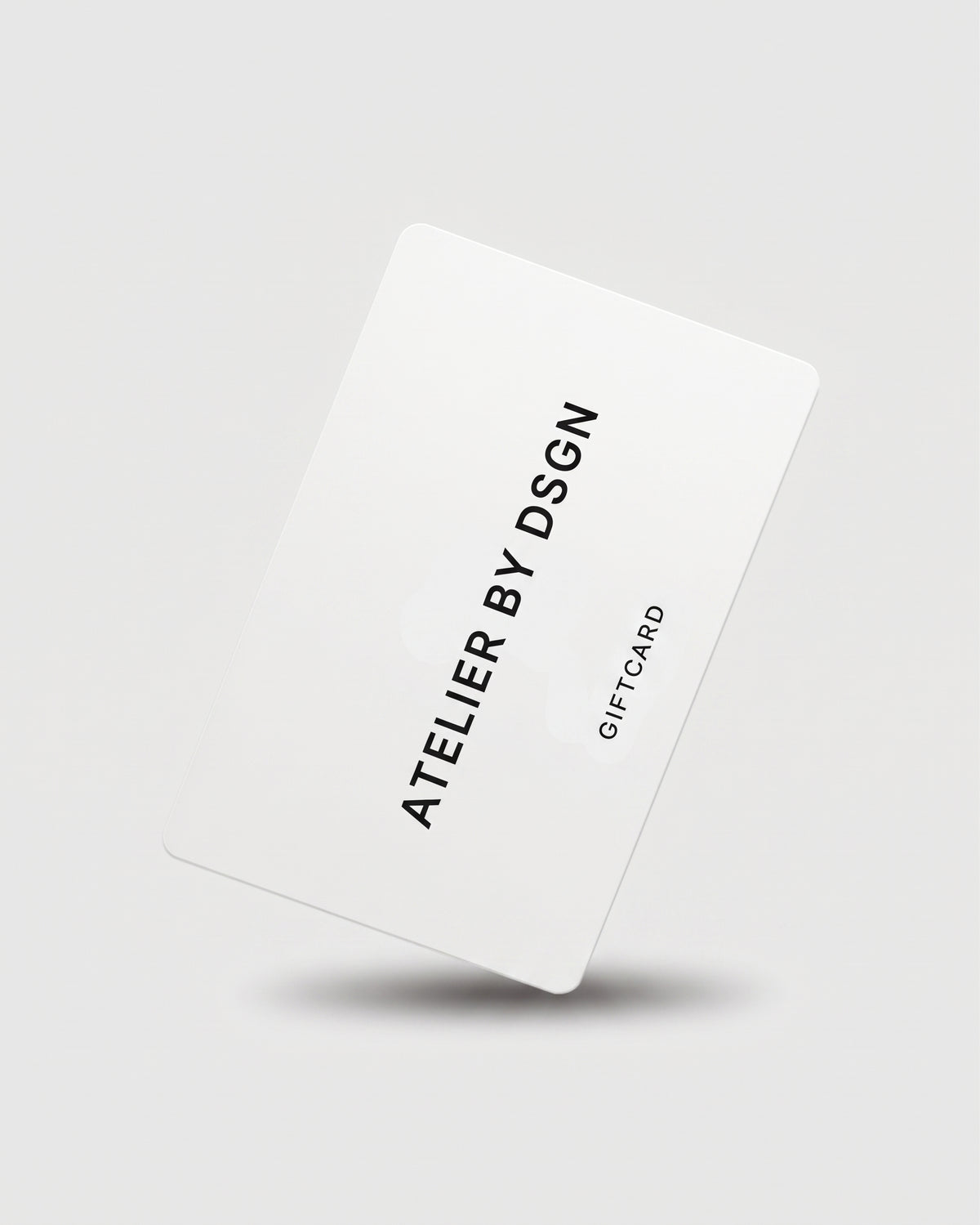 A white gift card with black text reading 'ATELIER BY DSGN' and 'GIFT CARD' on a light gray background with a soft shadow underneath.