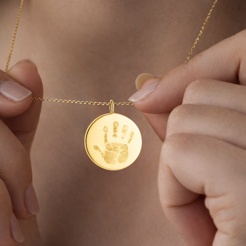 Female model holding custom engraved 18k gold vermeil 16mm coin pendant necklace at neckline displaying personalised baby handprint with intricate finger and palm detail precision diamond-head engraved on warm lustrous gold disc on delicate gold diamond-cut cable chain – Atelier By Dsgn luxury custom handprint coin necklace heartfelt gift for new mum, mothers day, baby shower, new baby arrival or treasured newborn family heirloom necklace