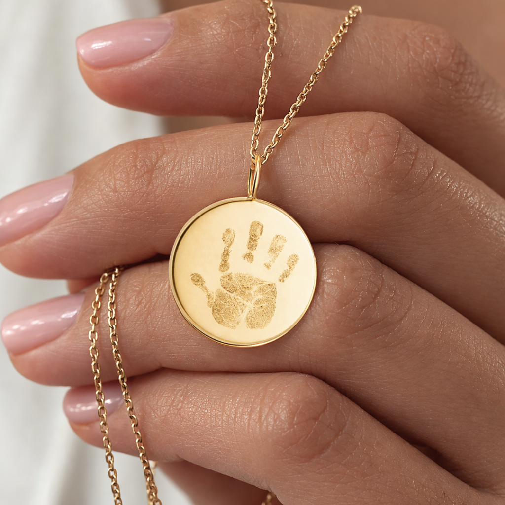 Close-up of custom engraved 18k gold vermeil 16mm coin pendant necklace resting in female palm with nude nails, showcasing intricate personalised baby handprint with detailed finger and palm texture precision diamond-head engraved on warm lustrous gold disc on delicate gold diamond-cut cable chain – Atelier By Dsgn luxury custom handprint coin necklace cherished gift for new mum, mothers day, baby shower, birth announcement or treasured newborn family heirloom necklace
