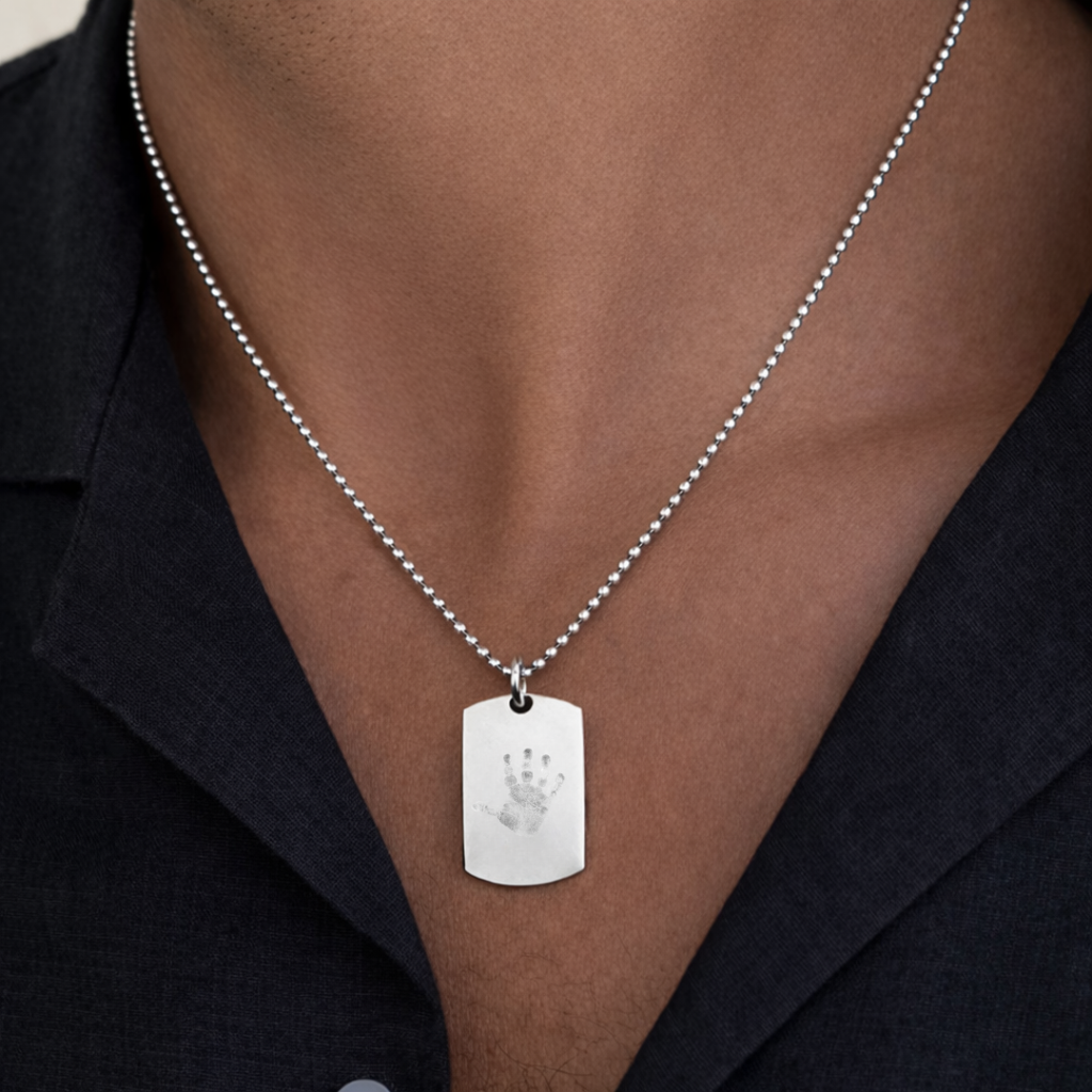 Custom engraved 925 sterling silver baby handprint dog tag necklace worn on male model in dark blazer, personalised child handprint with intricate finger detail precision diamond-head engraved on polished silver tag on 61cm bead chain – Atelier By Dsgn unisex custom handprint jewellery powerful gift for new dad, fathers day, new mum, baby arrival, child memorial or meaningful family keepsake necklace