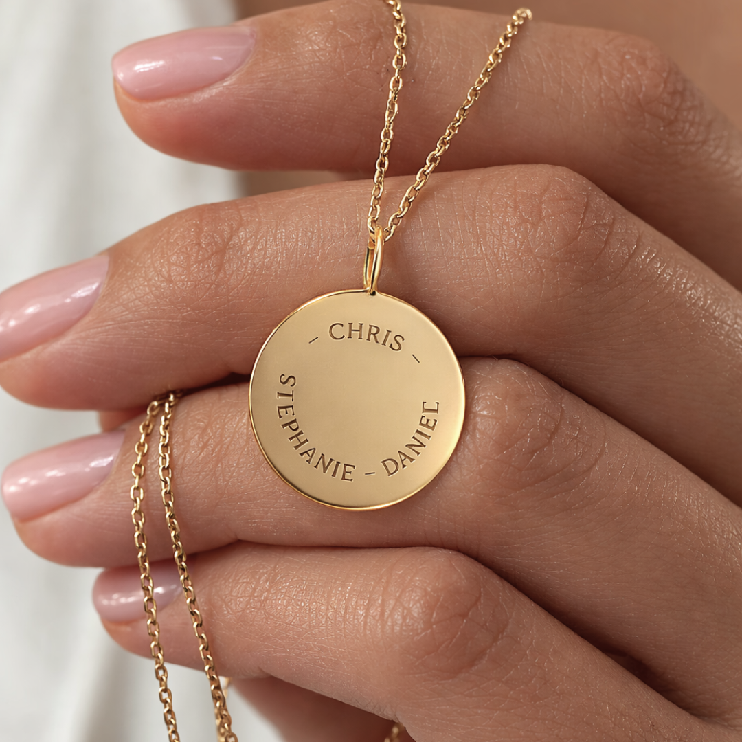 Close-up of custom engraved 18k gold vermeil 16mm coin pendant necklace held in female hand with nude nails, showcasing personalised family names "Chris, Stephanie, Daniel" precision diamond-head engraved in elegant curved layout on warm lustrous gold disc on delicate gold cable chain – Atelier By Dsgn luxury personalised text coin necklace meaningful gift for her, mothers day, family keepsake, anniversary or cherished custom names heirloom necklace