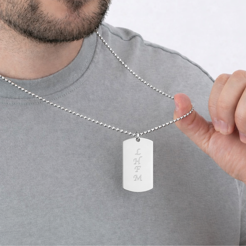 Male model in grey tee holding custom engraved 925 sterling silver personalised text dog tag necklace on 61cm bead chain, displaying stacked family initials "L, H, F, M" precision diamond-head engraved on polished silver tag – Atelier By Dsgn unisex personalised initials dog tag necklace everyday wear gift for dad, fathers day, family keepsake, anniversary or meaningful custom initials memorial necklace