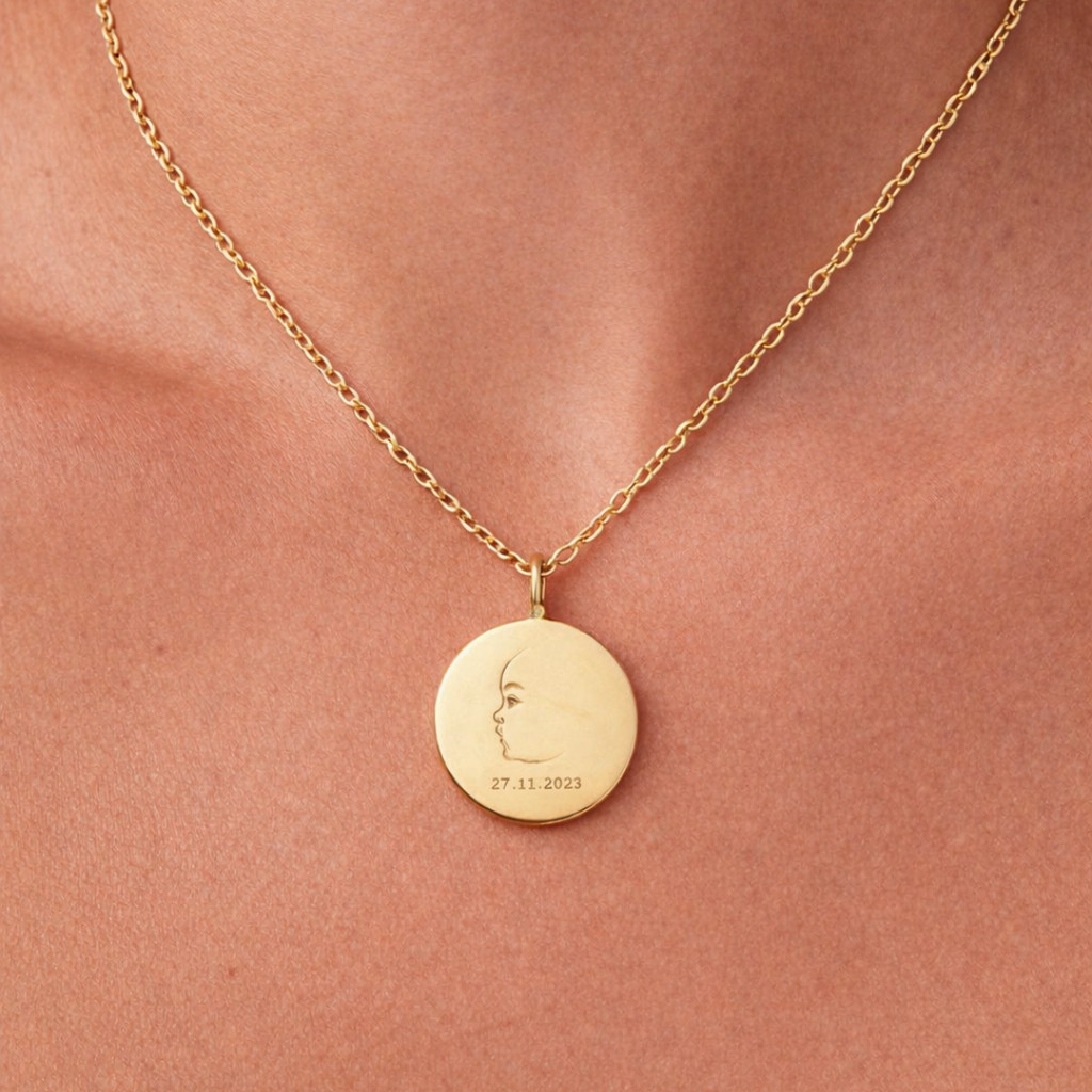 Custom engraved 18k gold vermeil 16mm coin pendant necklace worn at neckline on female model, personalised single-line minimalist newborn baby side profile portrait with birth date "27.11.2023" precision diamond-head engraved on warm lustrous gold disc on delicate diamond-cut cable chain – Atelier By Dsgn luxury custom baby portrait jewellery deeply personal gift for new mum, mothers day, baby shower or treasured newborn birth keepsake necklace