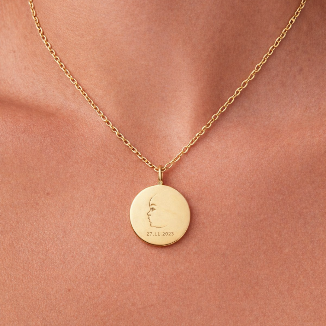 Custom engraved 18k gold vermeil 16mm coin pendant necklace worn at neckline on female model, personalised single-line minimalist newborn baby side profile portrait with birth date "27.11.2023" precision diamond-head engraved on warm lustrous gold disc on delicate diamond-cut cable chain – Atelier By Dsgn luxury custom baby portrait jewellery deeply personal gift for new mum, mothers day, baby shower or treasured newborn birth keepsake necklace