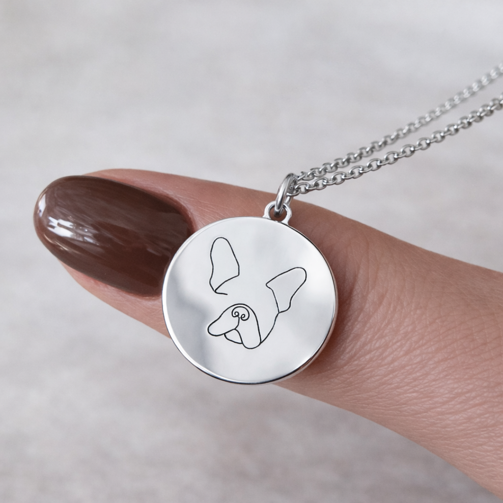 Close-up of custom engraved 925 sterling silver single-line drawing coin pendant necklace balanced on female fingertip with dark mauve nails, showcasing intricate personalised minimalist French Bulldog face portrait precision diamond-head engraved on high-polish round disc – Atelier By Dsgn custom pet portrait jewellery unique gift for dog lovers, French Bulldog mum, dog dad, pet memorial or cherished new puppy keepsake necklace