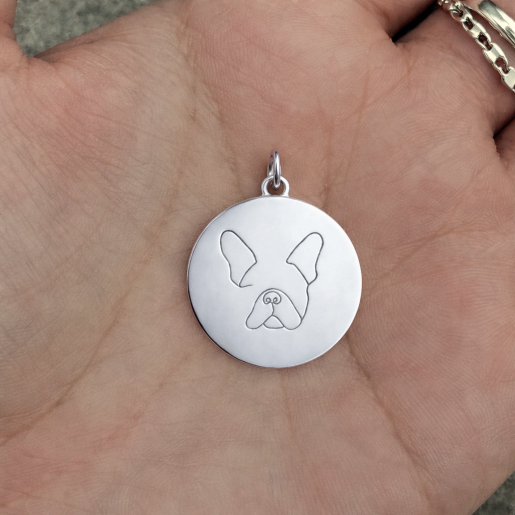 Custom engraved 925 sterling silver single-line drawing coin pendant held in open palm showing true size reference, personalised minimalist French Bulldog face portrait precision diamond-head engraved on high-polish round disc – Atelier By Dsgn custom pet portrait jewellery handcrafted gift for dog lovers, French Bulldog mum, dog dad, pet memorial or beloved new puppy celebration keepsake necklace