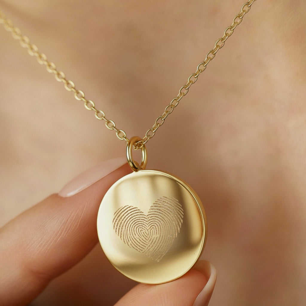 Close-up of the Heart Fingerprint Necklace in 18K Gold Vermeil by 
Atelier By DSGN, delicately held near the neckline. The pendant features two fingerprints forming a heart, symbolising love and connection. A fine, handcrafted personalised keepsake made with premium gold vermeil for timeless elegance.