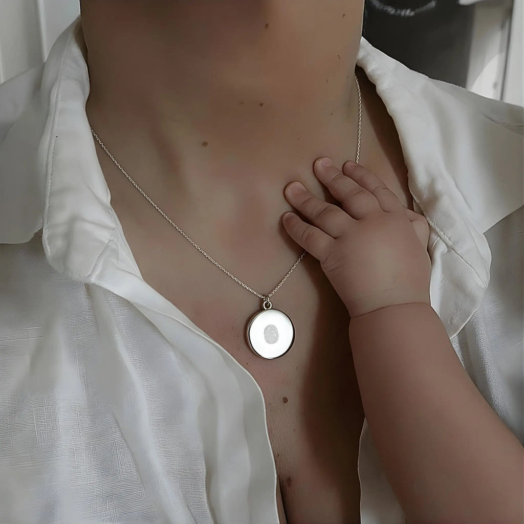A touching moment showing a mother wearing the Atelier By DSGN Single Fingerprint Pendant Necklace in 925 Sterling Silver while a baby’s hand gently touches it — a symbol of love, memory, and everlasting connection captured in fine personalized jewelry.