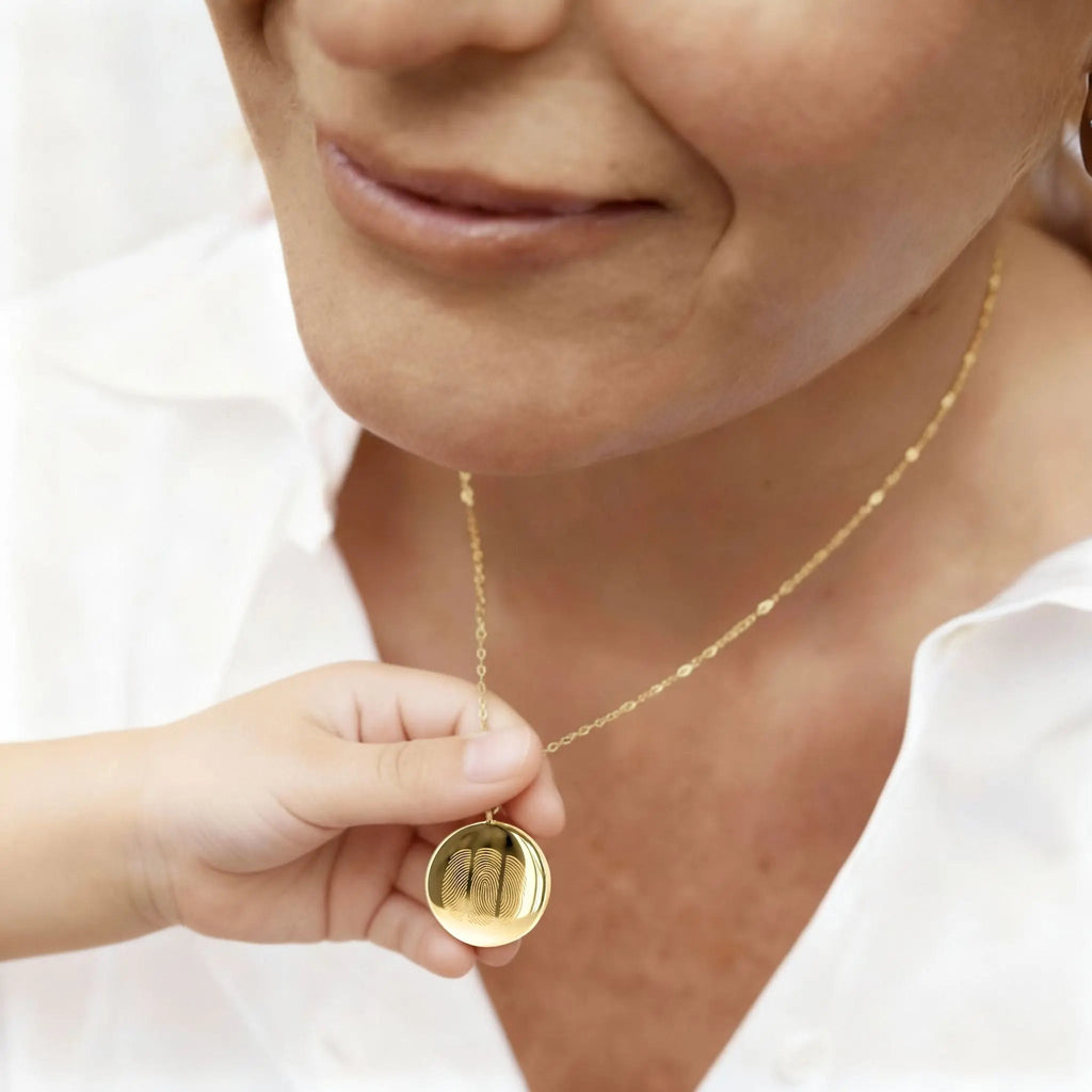 Emotional close-up of a mother and child holding the  Atelier By DSGN  Fingerprint Coin Necklace in 18K Gold Vermeil. The pendant features three engraved fingerprints symbolising family, love, and connection, a timeless keepsake capturing the bond between mother and child in luxurious, personalised detail.