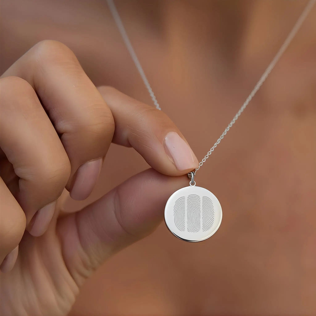 Close-up of a person holding the Atelier  By DSGN Three Fingerprint Pendant Necklace in 925 Sterling Silver, showing three engraved fingerprints on a polished round coin pendant — a personalized symbol of love, memory, and connection.