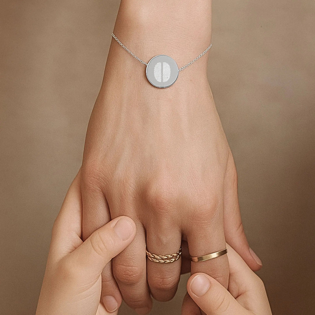 Close-up of a hand wearing the Atelier By DSGN Two Fingerprint Coin Bracelet in 925 Sterling Silver, held gently by a child’s hands — symbolising love, connection, and the lasting bond between generations.