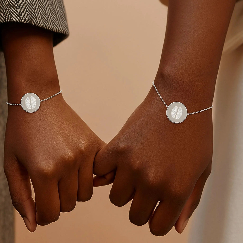 Two hands wearing matching Atelier By DSGN Two Fingerprint Coin Bracelets in 925 Sterling Silver, featuring engraved dual fingerprints on polished pendants, symbolising love, connection, and timeless togetherness.