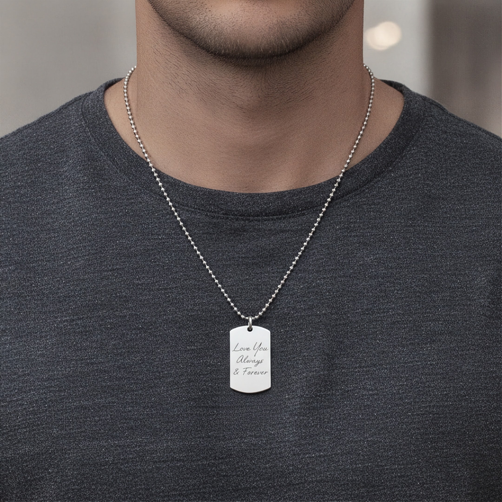 A silver bead chain necklace with a rectangular  custom hand writing engraved dog tag pendant reading 'Love You Always & Forever', worn by a man in a dark gray t-shirt.  Handwriting custom jewelry in sterling silver from Atelier By DSGN.