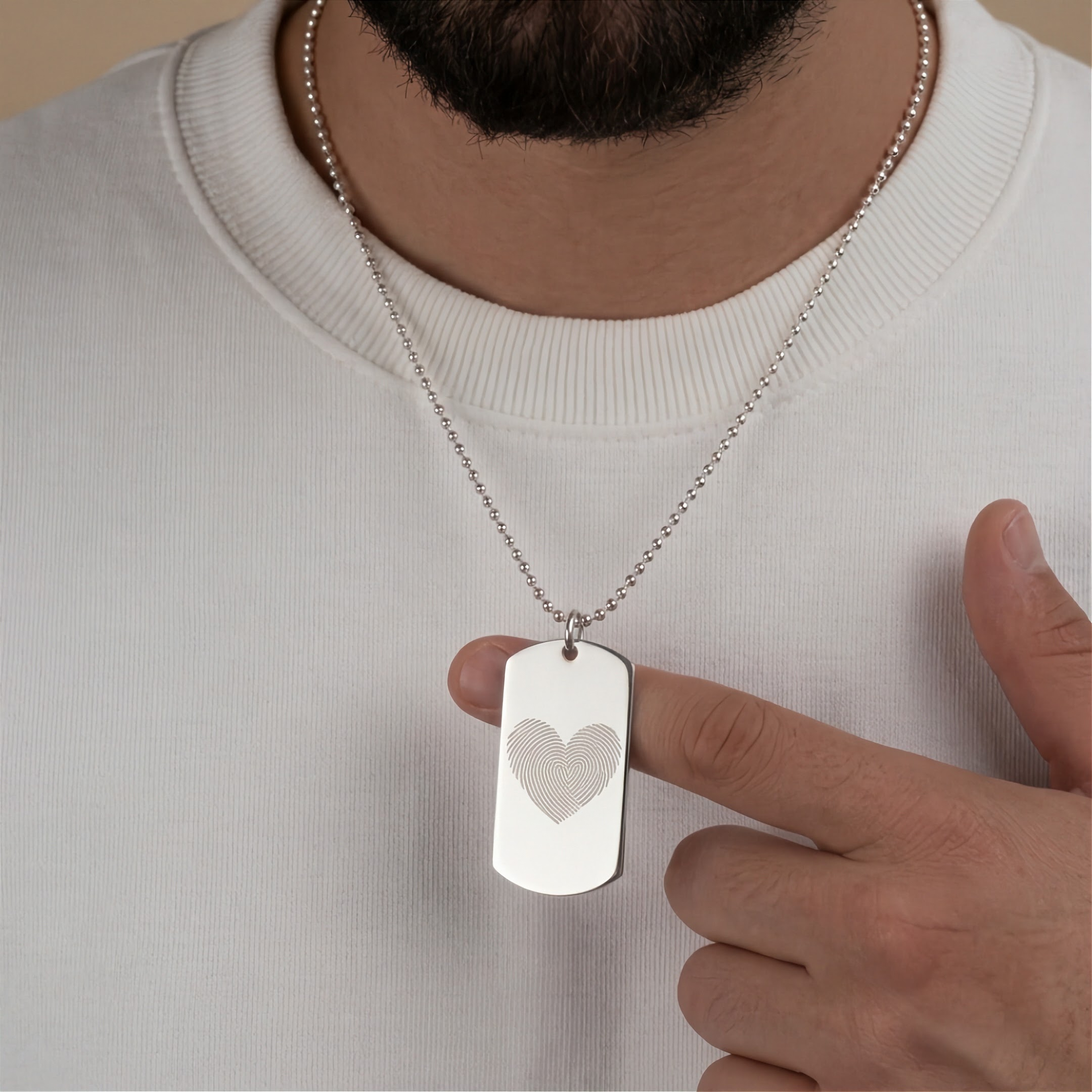 Heart fingerprint entraved dog tag pendant in sterling silver around a man's neck who is wearing a white Tshirt.  Custom jewelry from Atelier By DSGN.