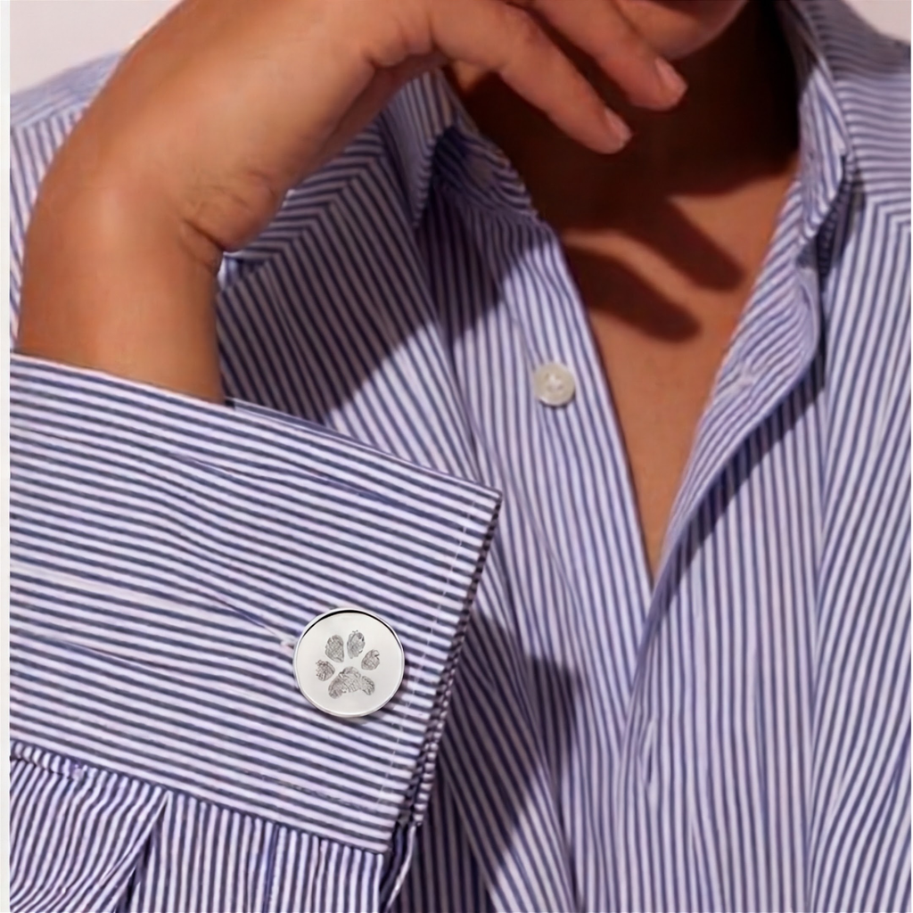 Close-up of a person wearing a blue and white vertically striped button-down shirt, featuring a sterling silver paw print engraved cufflink.  Custom engraved personal jewelry from Atelier By DSGN.