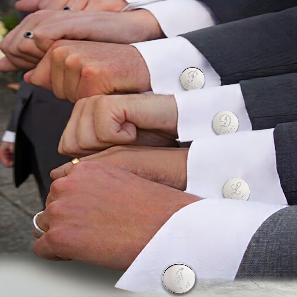 A close-up of multiple white dress cuffs on groomsman with round silver coin cuffed links featuring engraved monogram initials and engraved date at the bottom worn on a person's wrists with dark gray suit jackets.  Wedding cufflinks from Atelier By DSGN.