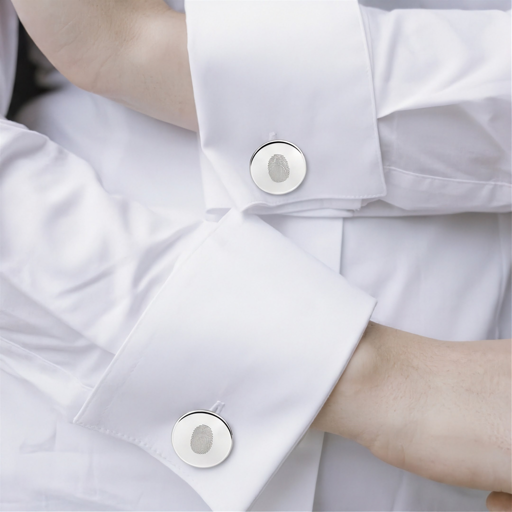 Close-up of a white dress shirt with two matching single sterling silver fingerprint engraved cufflinks and visible skin at the wrists.  Fingerprint jewelry from Atelier By DSGN