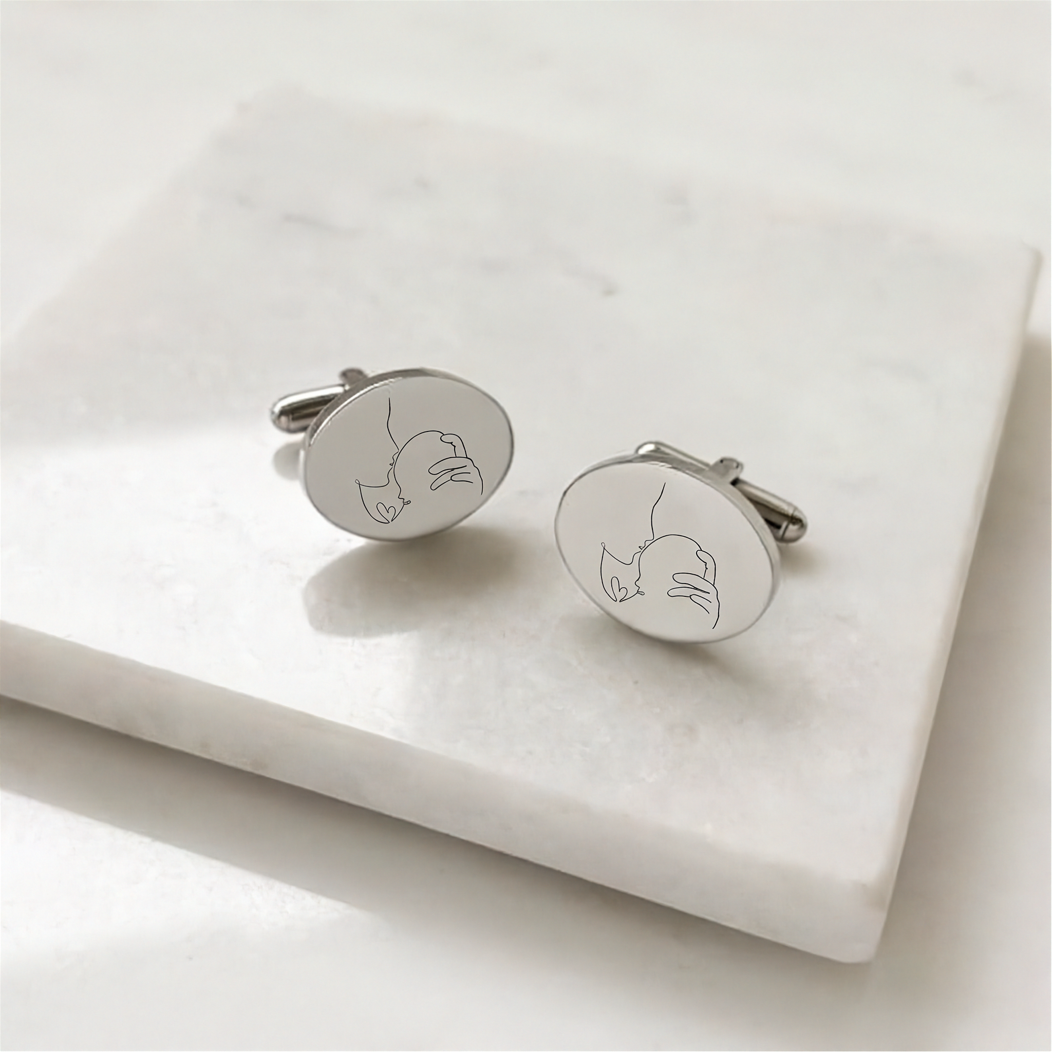 custom line art portrait engraved  coin cufflinks in sterling silver on a marble display table.  Engraving is of a lady holding her new born baby in beautiful line art.  Personalised cufflinks from Atelier By DSGN.