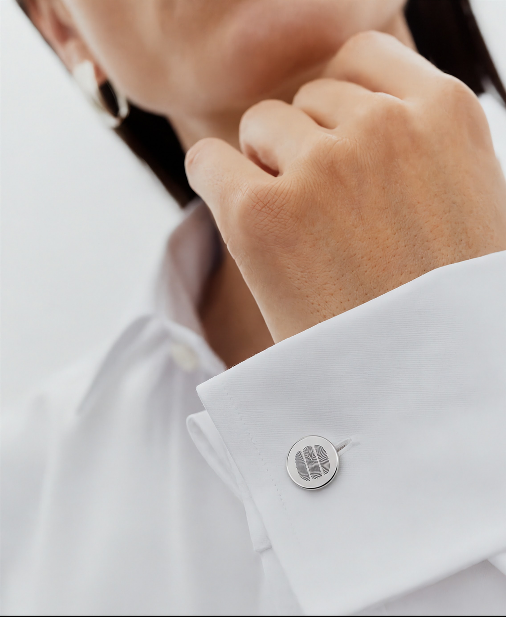 A close-up of a person wearing a white dress shirt with a 925 sterling silver cufflink featuring a three fingerprint design, against a clean white background.  Atelier By DSGN custom jewelry