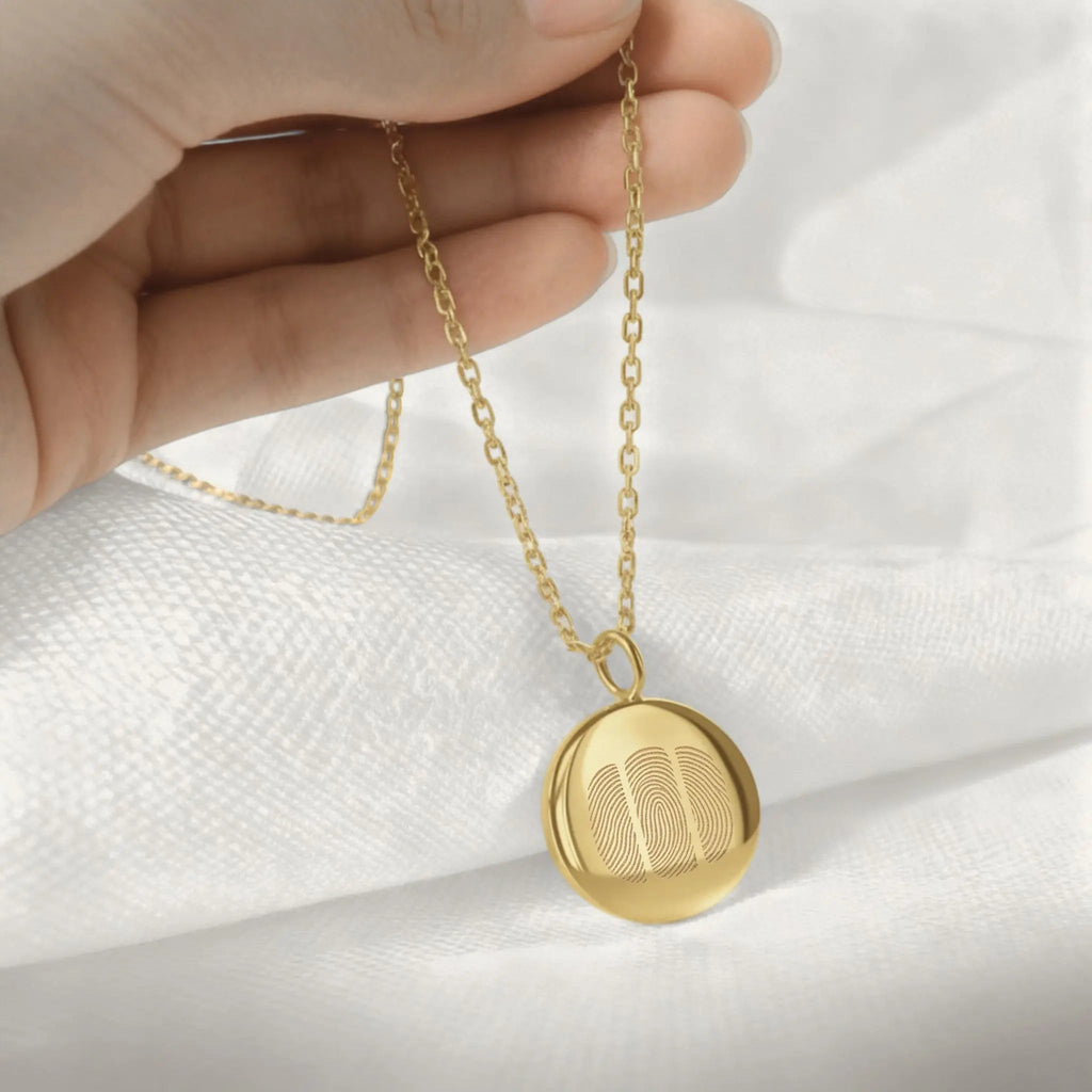 Hand holding the Luxury Three Fingerprint Coin Necklace in 18K Gold Vermeil by Atelier By DSGN. Features three delicately engraved fingerprints on a radiant gold pendant, symbolizing family bonds and connection. A timeless, personalized keepsake handcrafted for elegance and meaning.