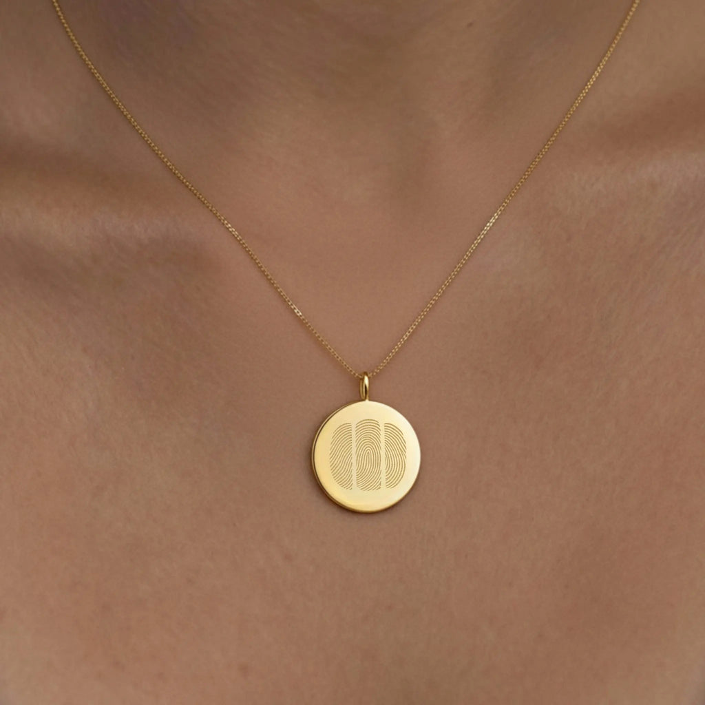 Model wearing the Luxury Three Fingerprint Coin Necklace in 18K Gold Vermeil by Atelier By DSGN. The engraved triple fingerprint design sits elegantly against the skin, symbolizing lasting connection and love. A modern, personalized heirloom crafted in radiant gold vermeil for everyday luxury.