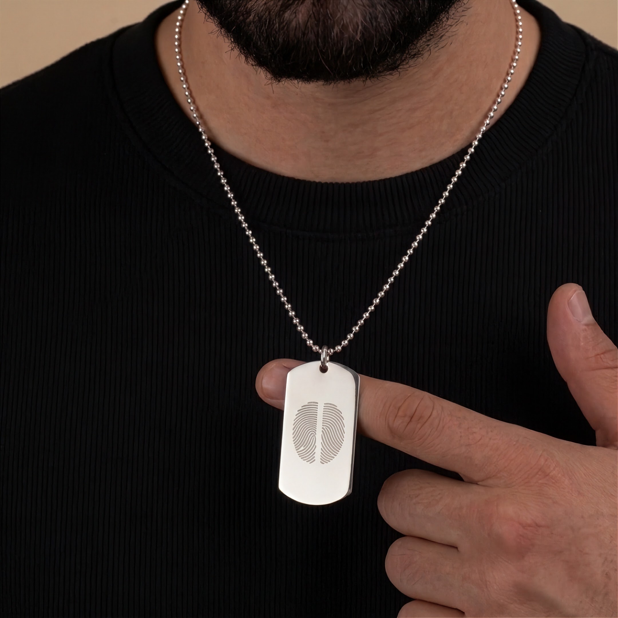 A 925 sterling silver dog tag pendant necklace with a two fingerprint engraved design, worn by a man in a black T-shirt.  Custom jewelry from Atelier By DSGN.