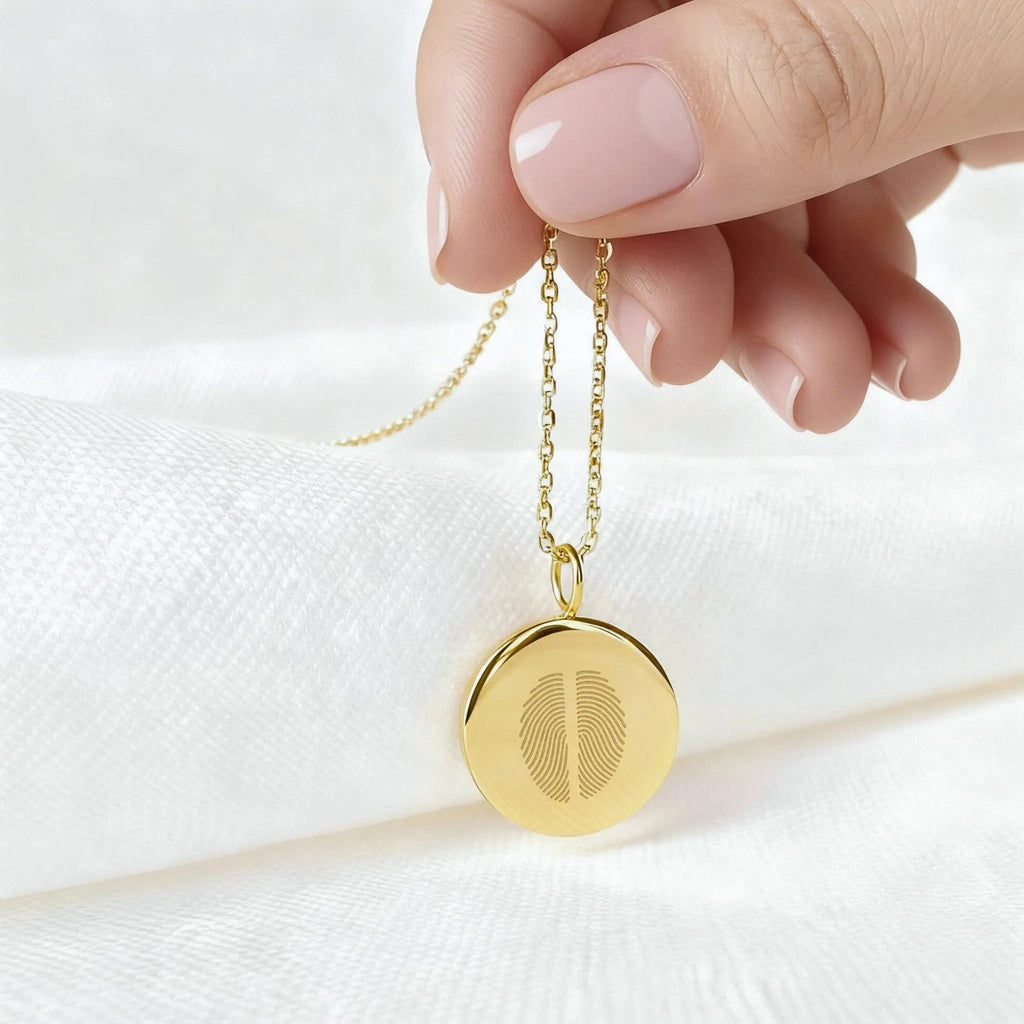Handheld two fingerprint pendant necklace in 18K gold vermeil by Atelier By DSGN,, featuring dual engraved fingerprints on a polished round disc. A luxury, sentimental keepsake celebrating meaningful connections, handcrafted for timeless elegance and personalization.